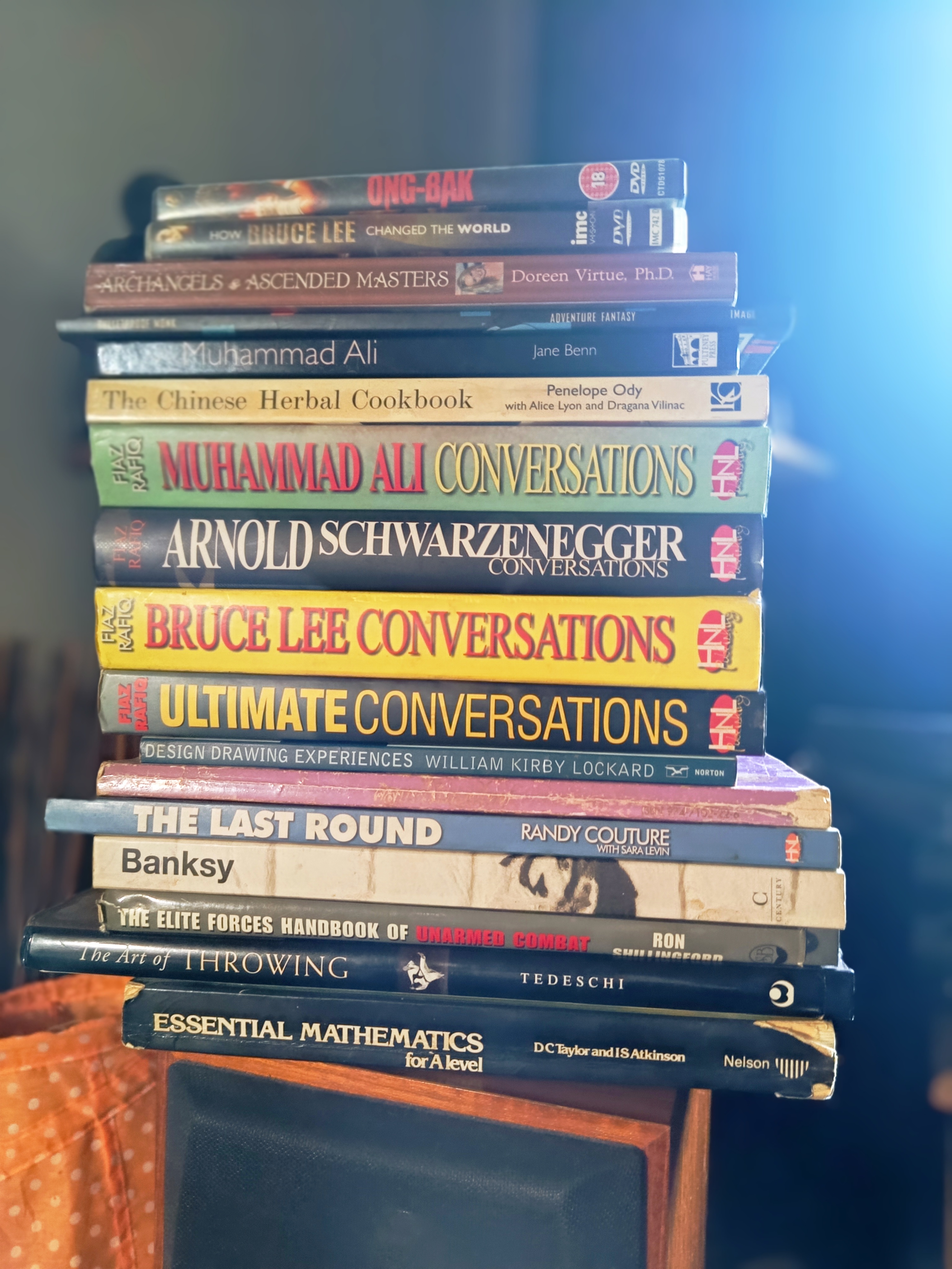 Stack of books including Bruce Lee Conversations, Muhammad Ali, Arnold Schwarzenegger, Randy Couture The Last Round, Banksy, Art of Throwing, A-Level Maths