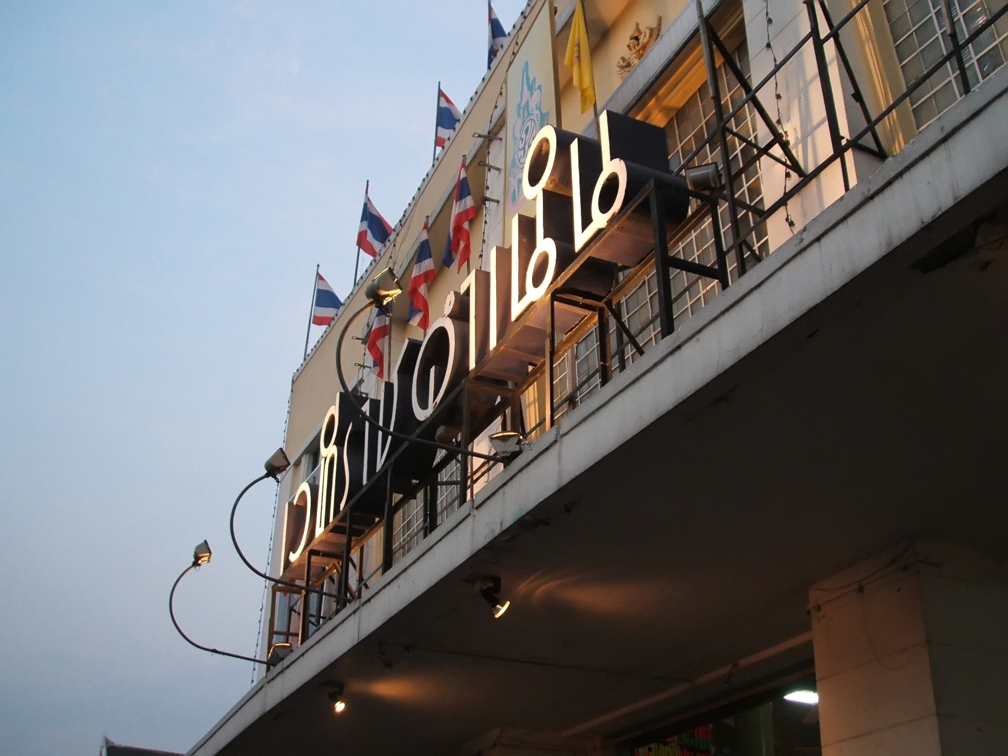 Ratchadamnern Stadium exterior at dusk, Thai script signage illuminated, Thai flags flying