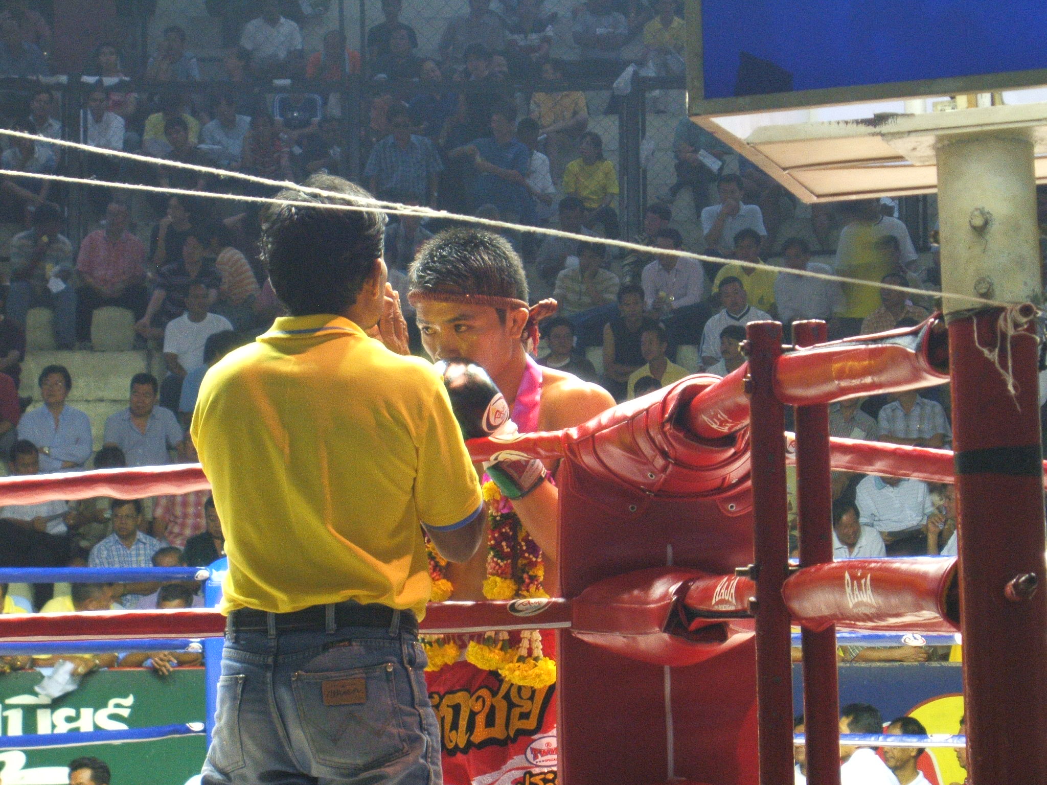 A Thai fighter wearing mongkhon headband and garlands receiving instructions from trainer at Ratchadamnern Stadium