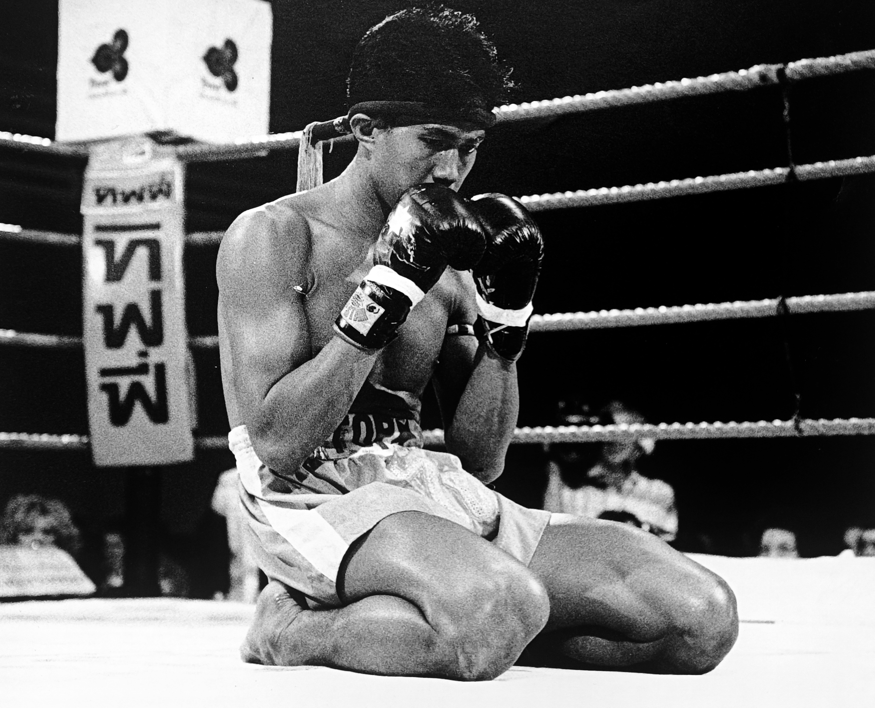 A Thai opponent kneeling on the canvas wearing a mongkhon headband after being knocked down by Ronnie