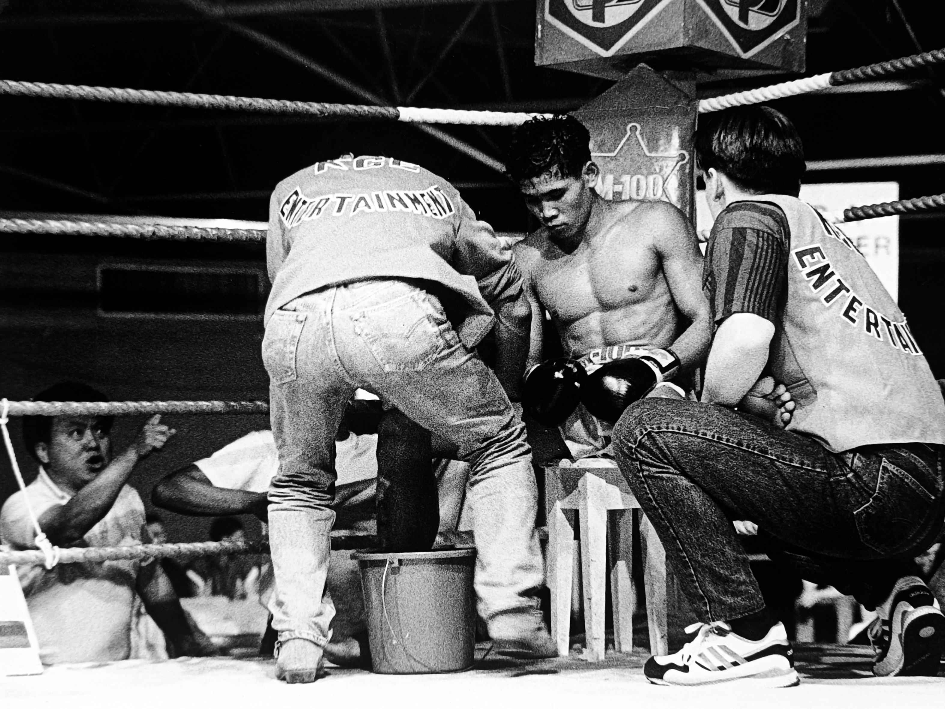 A young Thai fighter sitting on his stool between rounds, KGB Entertainment corner men working on him