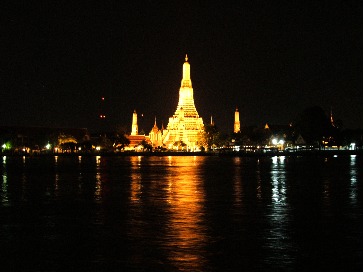 Wat Arun temple lit up golden at night, reflected in the Chao Phraya river